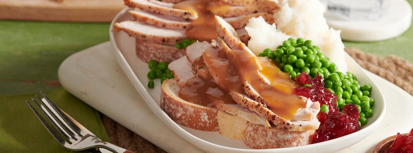 Open-faced hot turkey sandwich with gravy served with side of peas, mashed potatoes, and cranberry sauce