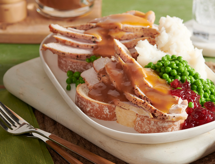 Open-faced hot turkey sandwich with gravy served with side of peas, mashed potatoes, and cranberry sauce